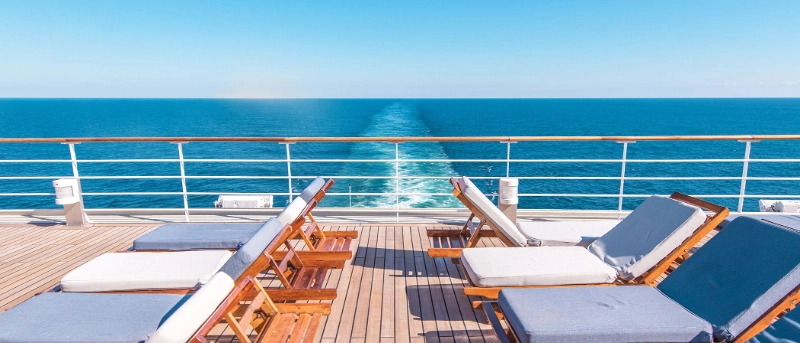 Lounge chairs on the open deck of a cruise ship overlooking the ocean and ship's wake
