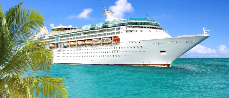 Large cruise ship sailing through clear turquoise tropical waters beside palm trees on a sunny day